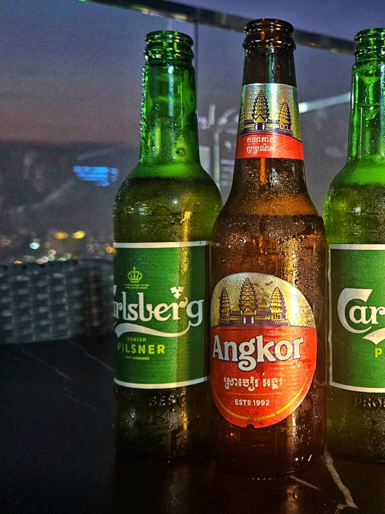 The Angkor beer that changed my travel. Picture of Angkor Beer Bottle with two Carlsberg Lager bottles behind, on table in a bar, Siem Reap, Cambodia