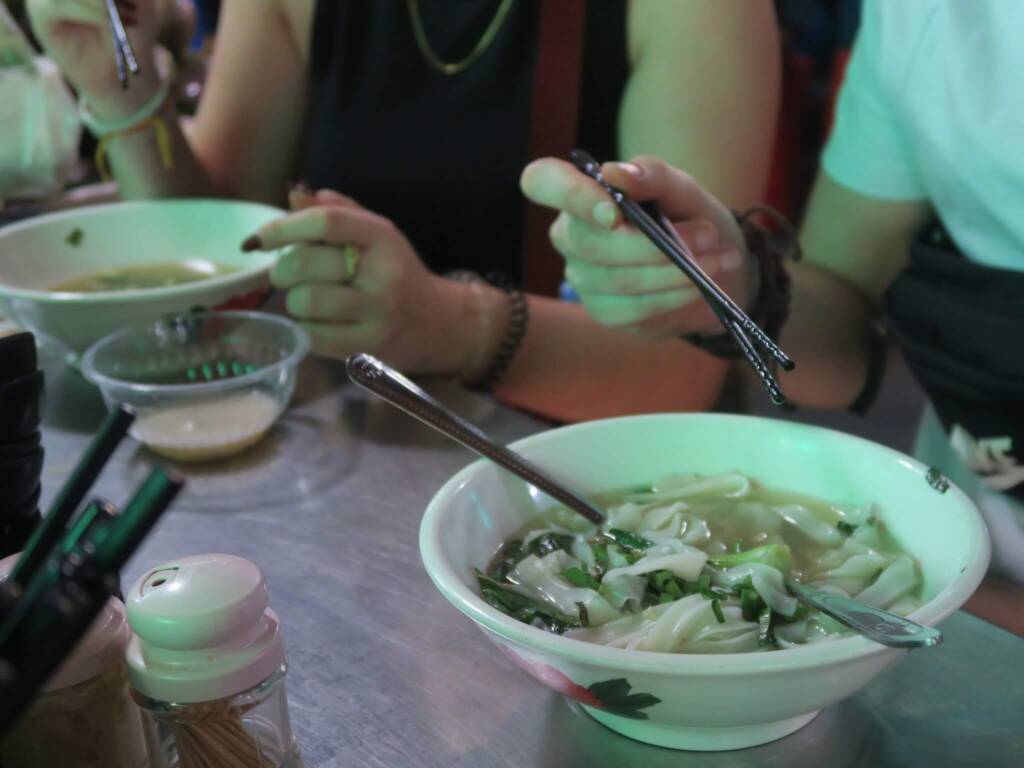 Backpackers enjoying pho (Vietnamese noodle soup) at a street food market in Southeast Asia