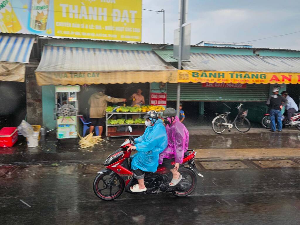 Locals on a motorbike wearing colorful rain ponchos during a heavy monsoon downpour in Ho Chi Ming City, Southeast Asia
