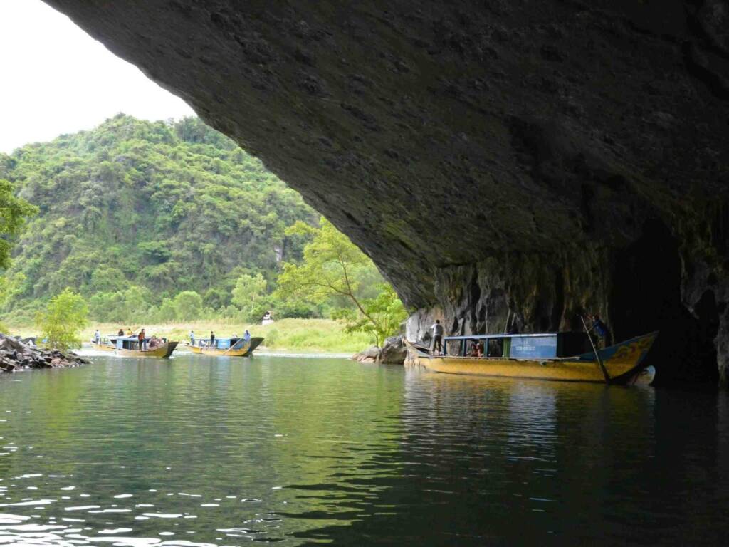 Long-tail boats entering the massive cave mouth in Phong Nha-Kẻ Bàng National Park, highlighting a hidden gem adventure in Central Vietnam.