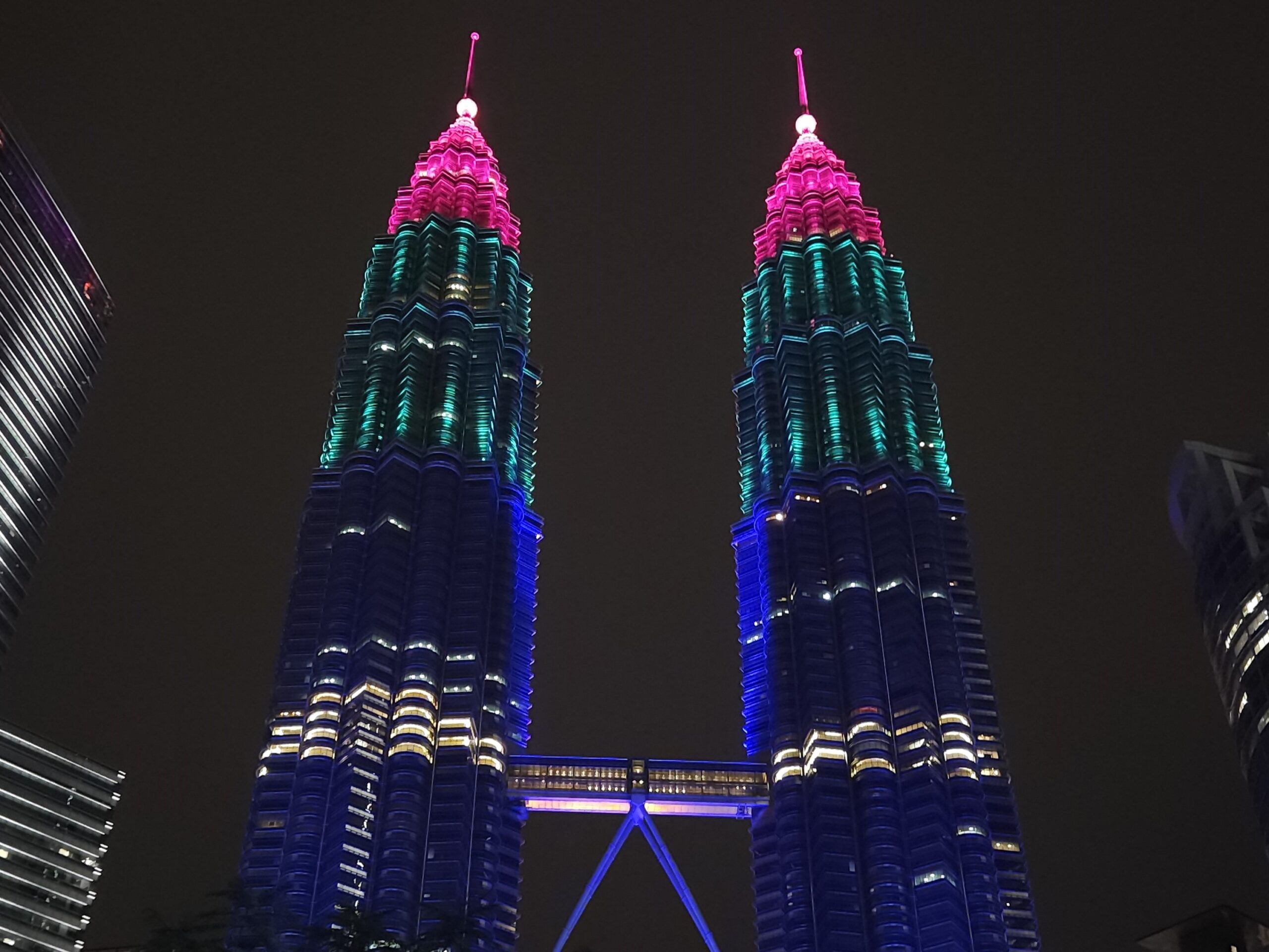 The Petronas Twin Towers illuminated with vibrant pink and blue lights at night in Kuala Lumpur, Malaysia.