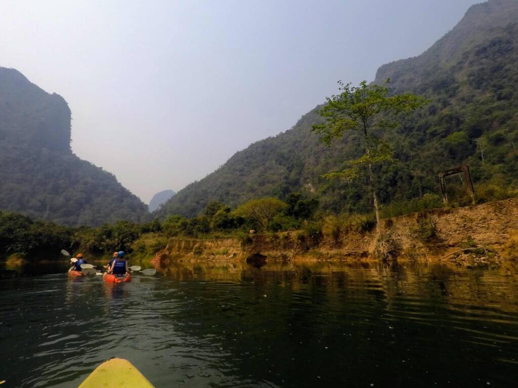 Backpackers kayaking on the Nam Ou River, surrounded by jungle mountains in Nong Khiaw, Laos, as part of a 6 month Southeast Asia itinerary.