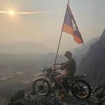 Backpacker celebrating on a motorbike with the Laos flag, overlooking the valley. Ultimate 6-month Southeast Asia itinerary.